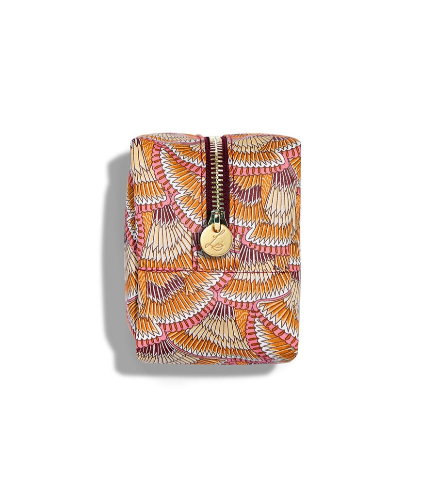 Side view of a rectangular beauty bag on a white background. The bag is made using Liberty print fabric which looks like overlapping fans that have brown, beige, orange, white and pink stripes. The bag has a gold circular zip tag with Lisa Eldridge’s logo on it.