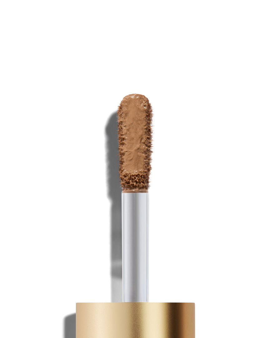 The end of a gold cap containing an applicator wand with a mauve beige Liquid Silk eyeshadow on it, against a white background.