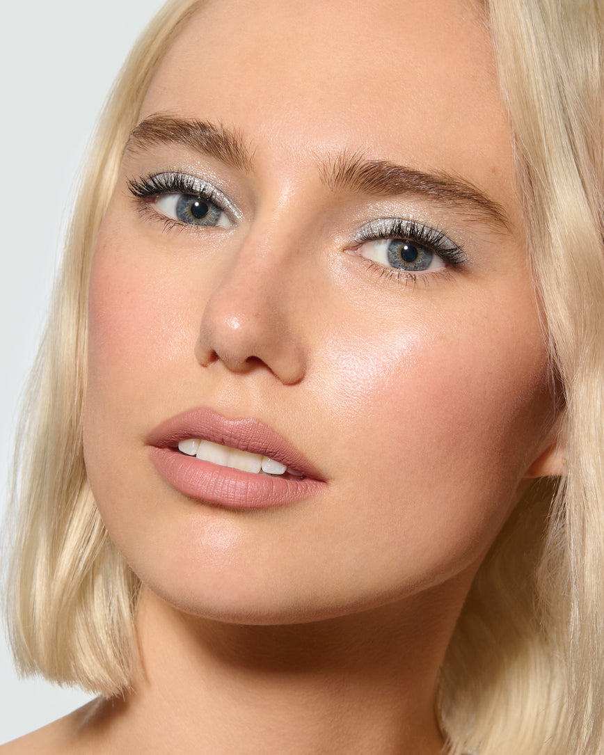 Close-up of a model's face, against a neutral background, wearing Aria Liquid Lurex Liquid Eyeshadow, a true, cool, clear silver.