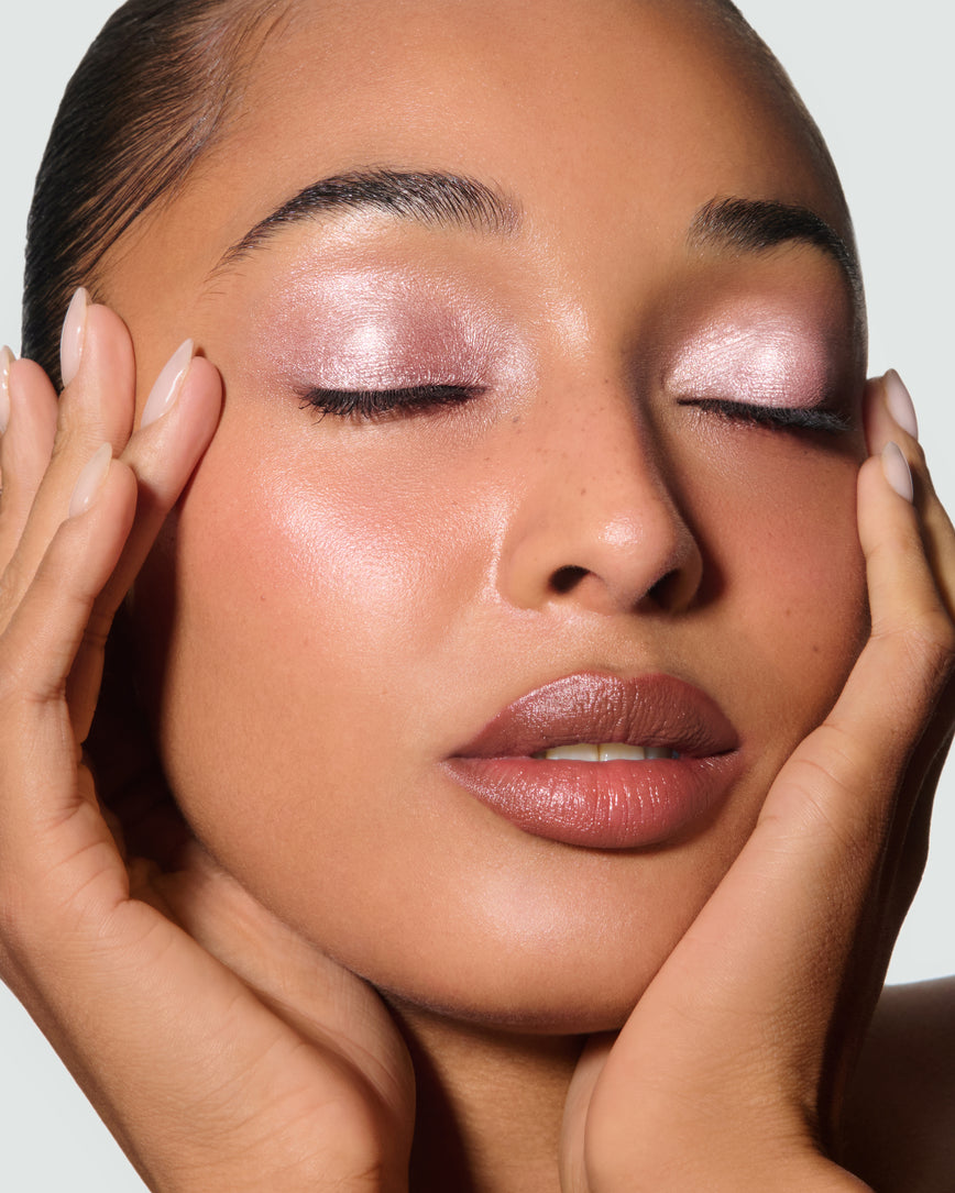 Close-up of a model's face against a neutral background, wearing Rosalie Liquid Lurex Liquid Eyeshadow, a warm, peachy rose.