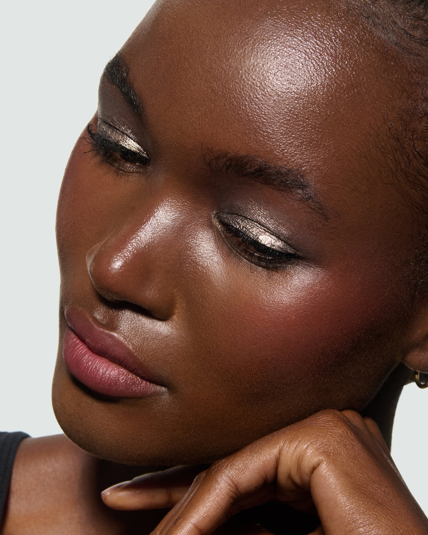 Close-up of a model's face against a neutral background, wearing Selene Liquid Lurex Liquid Eyeshadow, a tarnished, cool toned greenish/silver.