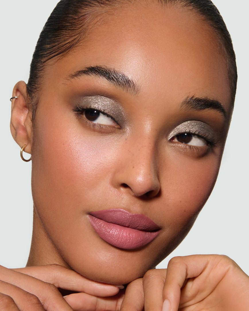 Close-up of a model's face against a neutral background, wearing Selene Liquid Lurex Liquid Eyeshadow, a tarnished, cool toned greenish/silver.