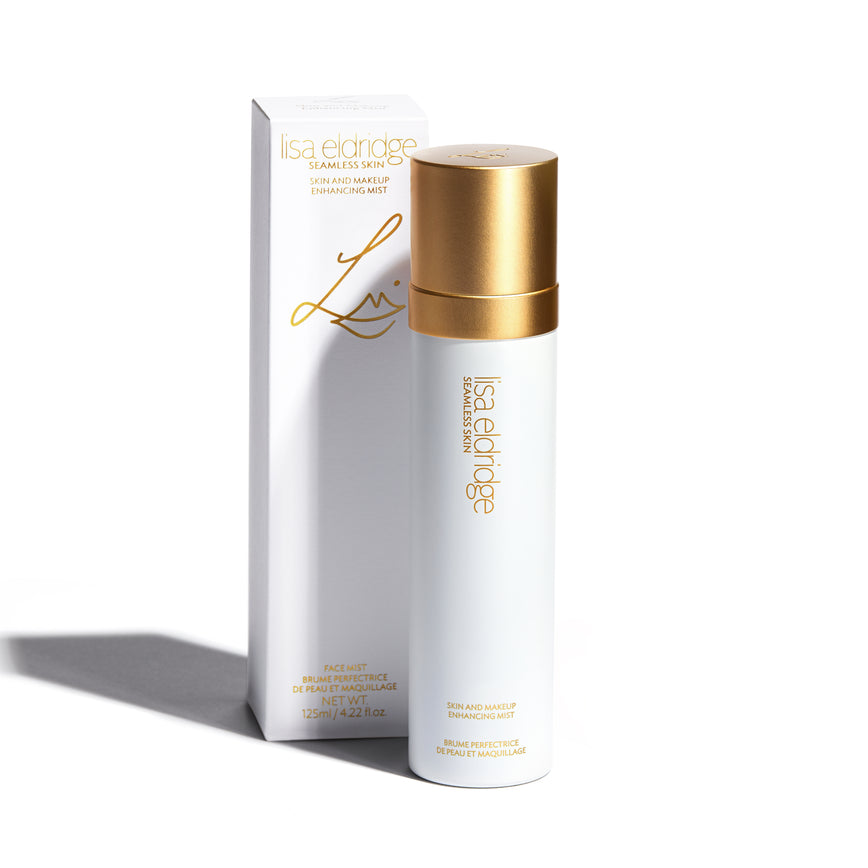 Lisa Eldridge Skin and Makeup Enhancing Mist bottle in white and gold, standing upright in front of cardboard packaging, also white and gold