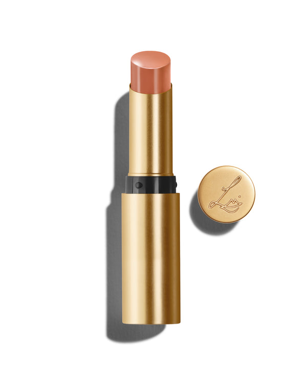 Baume Embrace in Meet Cute, a light peach lip colour, with a gold-colored casing, next to the Lisa Eldridge logo-embossed lid