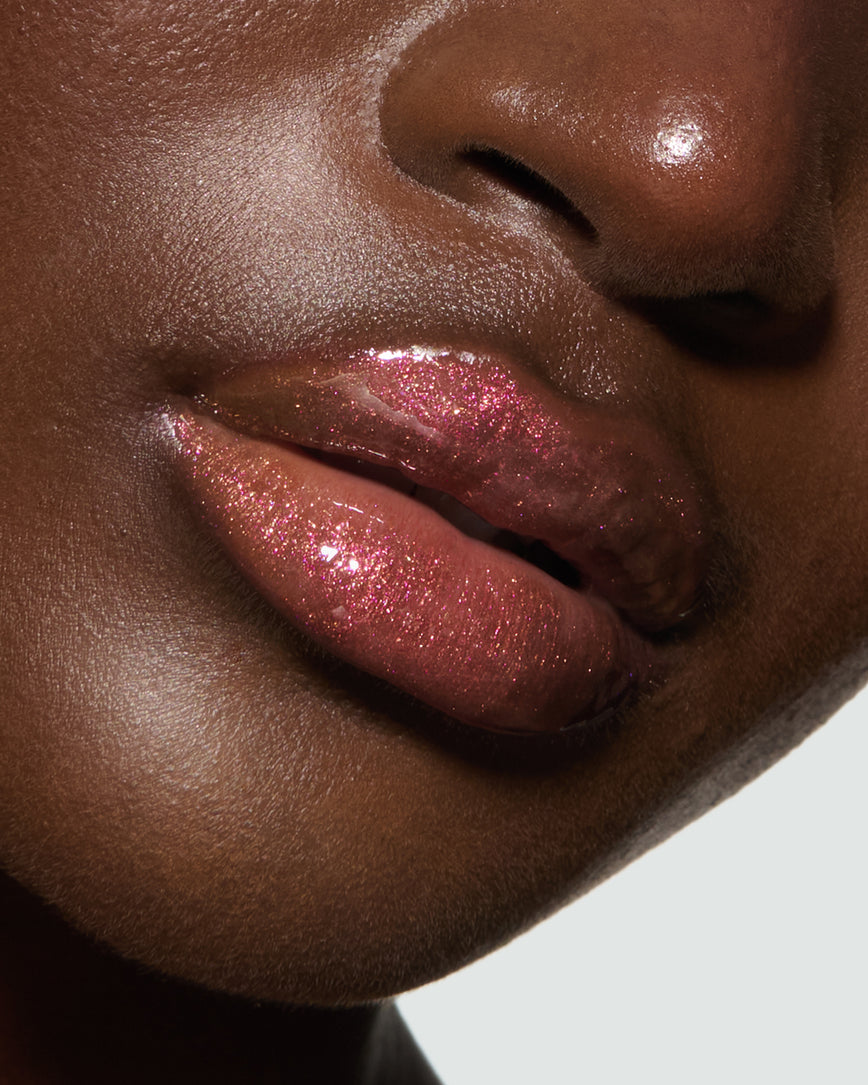 Close-up of a model's lips against a neutral background, wearing Chameleon Chaos Gloss Embrace Sequin, a burnt orange punch with duo-chrome orange-pink sparkle.
