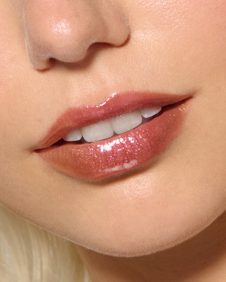 Close-up of a model's lips against a neutral background, wearing Chameleon Chaos Gloss Embrace Sequin, a burnt orange punch with duo-chrome orange-pink sparkle.