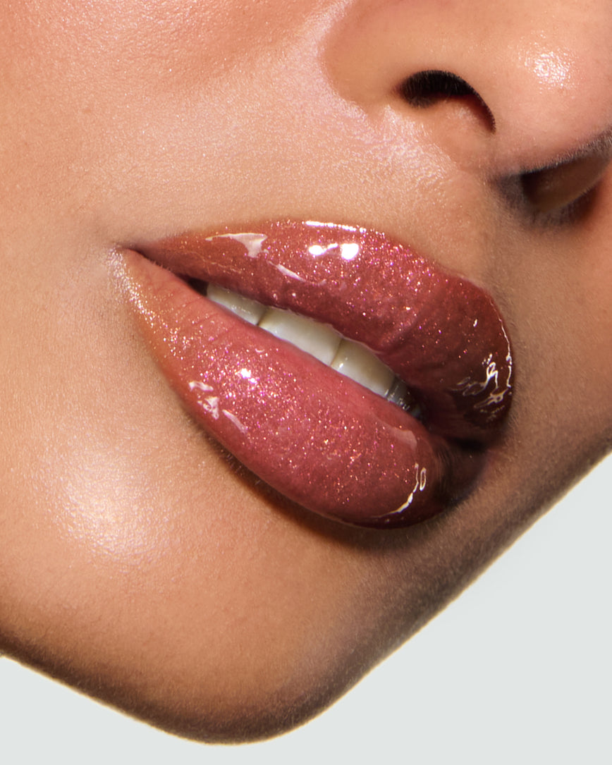 Close-up of a model's lips against a neutral background, wearing Chameleon Chaos Gloss Embrace Sequin, a burnt orange punch with duo-chrome orange-pink sparkle.