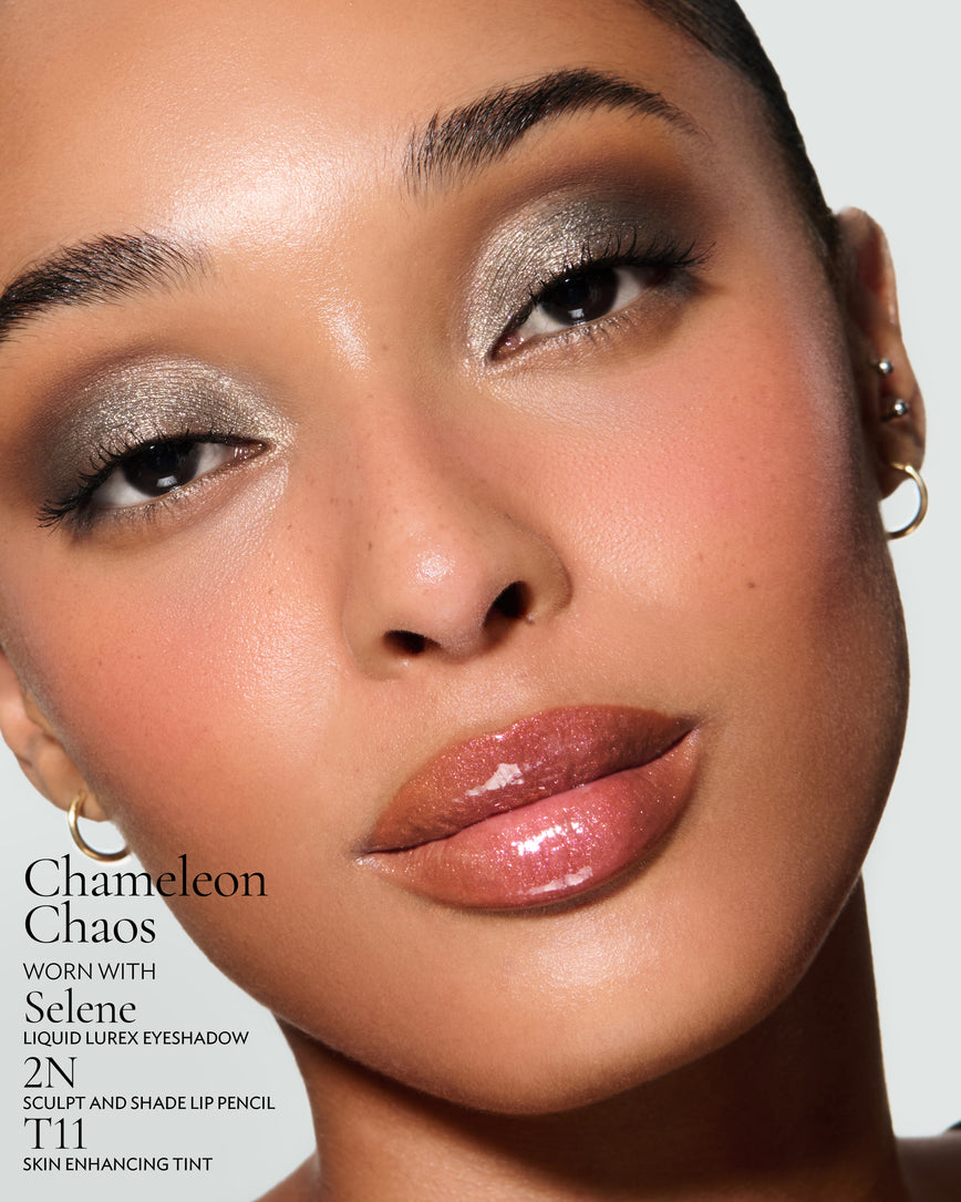 Close-up of a model's face against a neutral background, wearing Chameleon Chaos Gloss Embrace Sequin, with Selene Liquid Lurex, 2N Sculpt and Shade Pencil and T11 Skin Enhancing Tint.