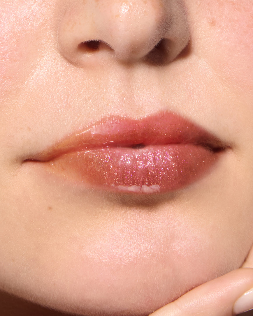Close-up of a model's lips against a neutral background, wearing Chameleon Chaos Gloss Embrace Sequin, a burnt orange punch with duo-chrome orange-pink sparkle.
