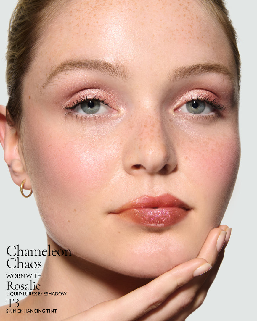 Close-up of a model's face against a neutral background, wearing Chameleon Chaos Gloss Embrace Sequin, with Rosalie Liquid Lurex, and T3 Skin Enhancing Tint.