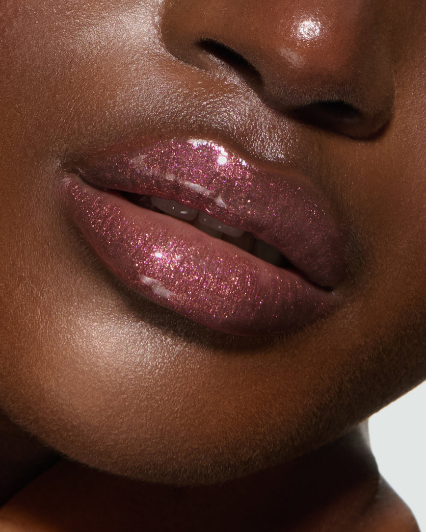 Close-up of a model's lips against a neutral background, wearing Kensington Plum Gloss Embrace Sequin, chocolatey plum berry with golden sparkle.