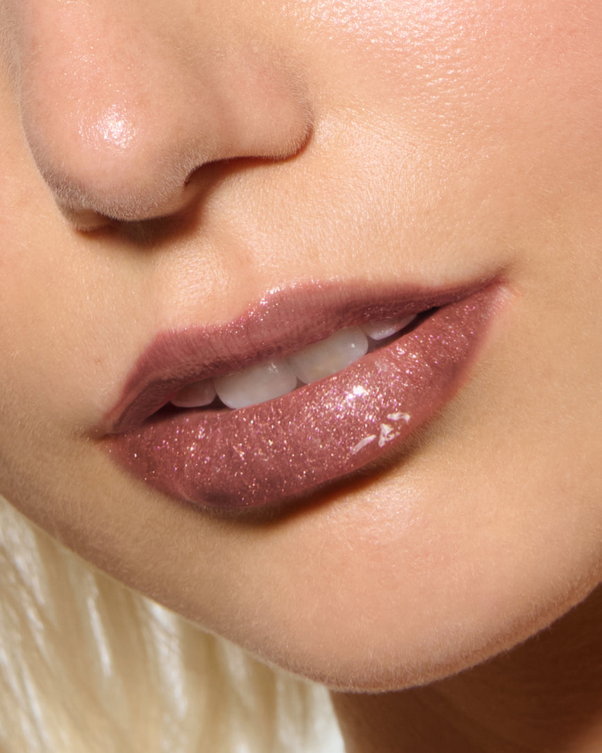 Close-up of a model's lips against a neutral background, wearing Chameleon Chaos Gloss Embrace Sequin, a burnt orange punch with duo-chrome orange-pink sparkle.