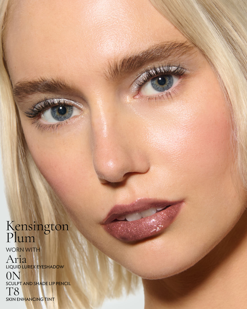 Close-up of a model's face against a neutral background, wearing Kensington Plum Gloss Embrace Sequin, with Aria Liquid Lurex, 0N Sculpt and Shade Pencil, and T8 Skin Enhancing Tint.