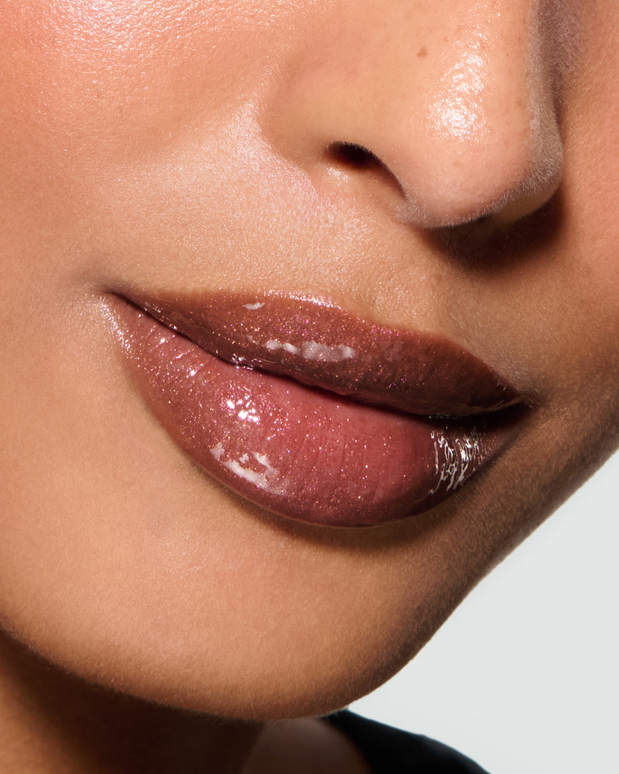 Close-up of a model's lips against a neutral background, wearing Kensington Plum Gloss Embrace Sequin, chocolatey plum berry with golden sparkle.