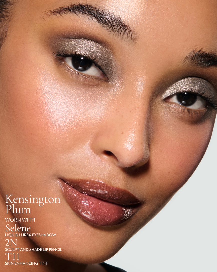 Close-up of a model's face against a neutral background, wearing Kensington Plum Gloss Embrace Sequin, with Selene Liquid Lurex, 2N Sculpt and Shade Pencil, and T11 Skin Enhancing Tint.