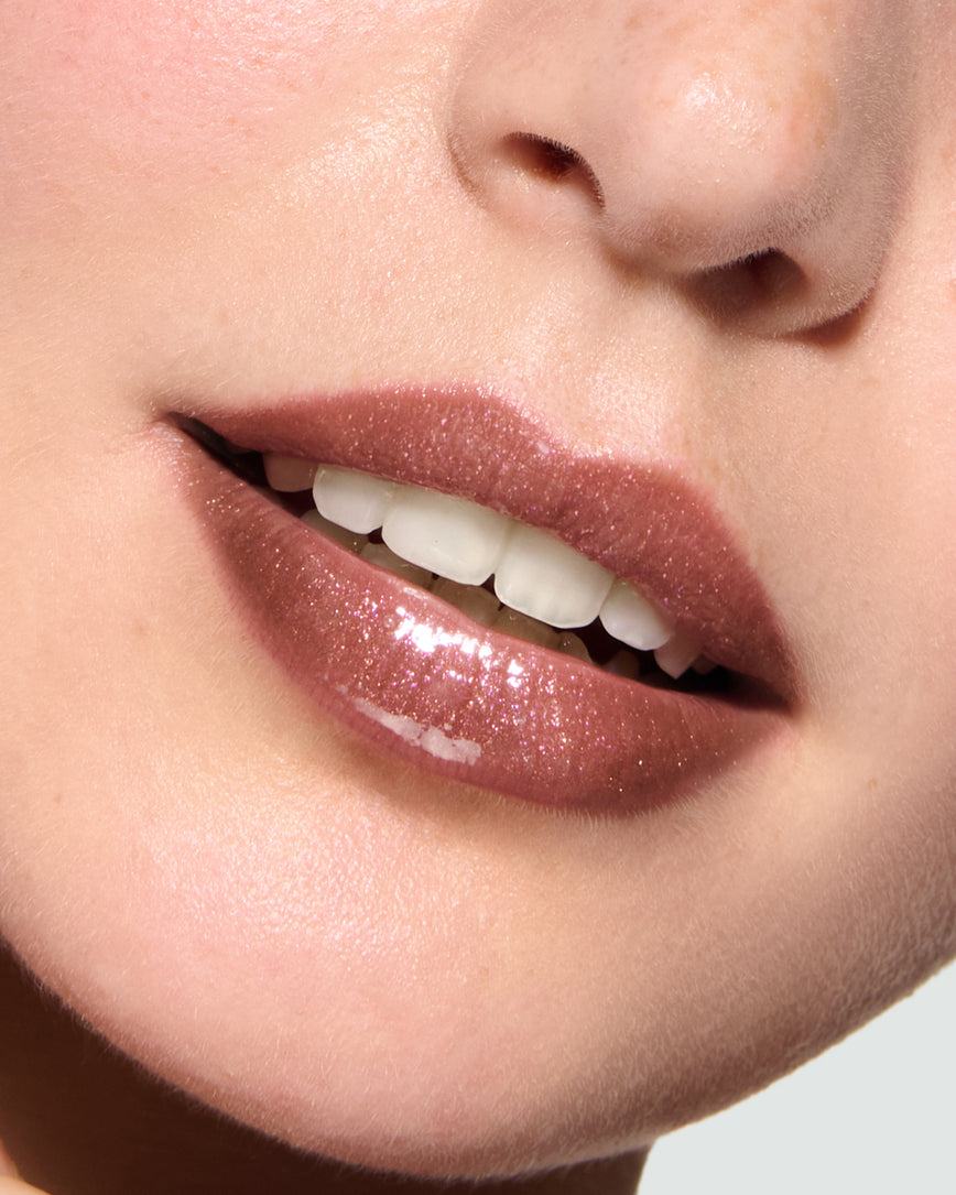 Close-up of a model's lips against a neutral background, wearing Kensington Plum Gloss Embrace Sequin, chocolatey plum berry with golden sparkle.