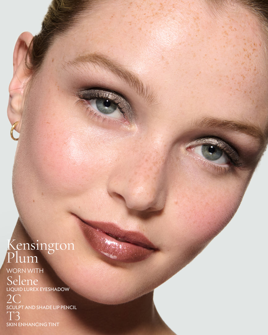 Close-up of a model's face against a neutral background, wearing Kensington Plum Gloss Embrace Sequin, with Selene Liquid Lurex, 2C Sculpt and Shade Pencil, and T3 Skin Enhancing Tint.