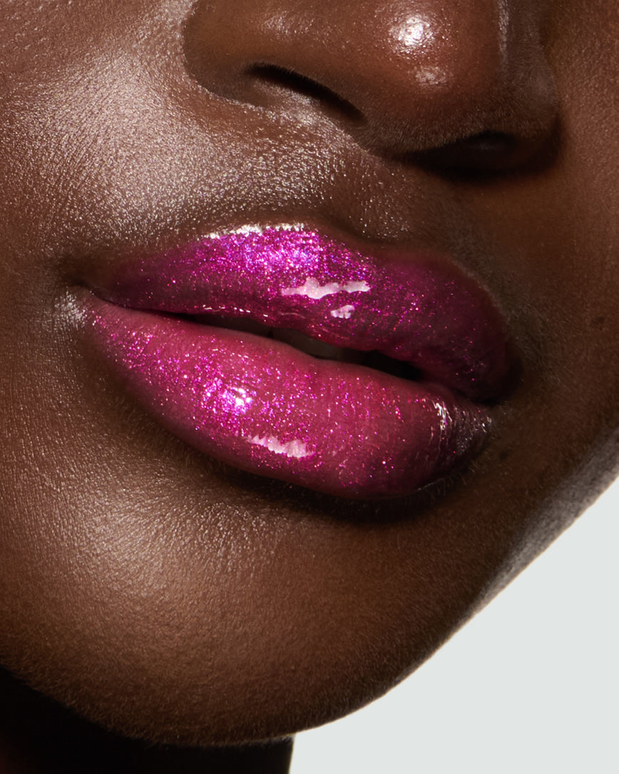 Close-up of a model's lips against a neutral background, wearing Peek-A-Boo Pink Gloss Embrace Sequin, chocolatey plum berry with golden sparkle.