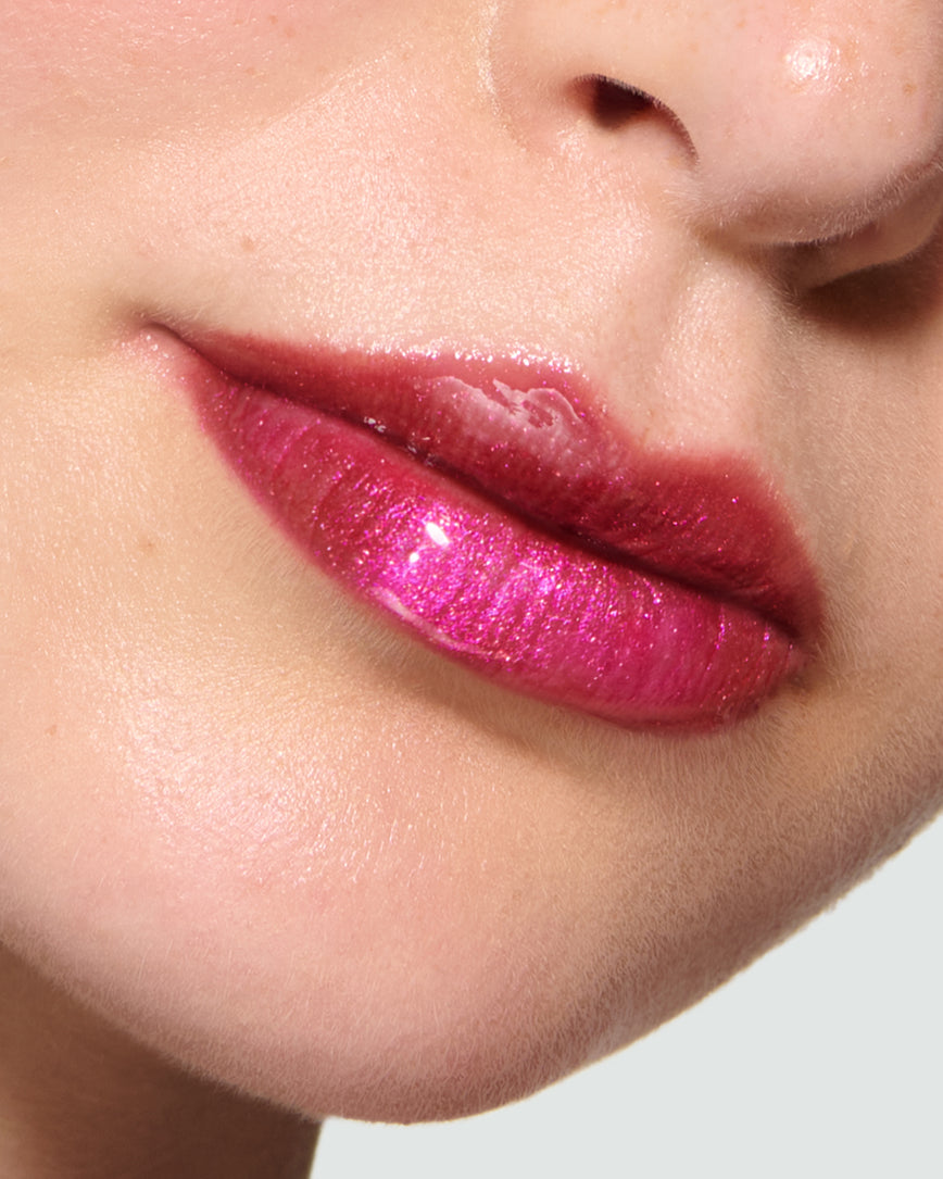 Close-up of a model's lips against a neutral background, wearing Peek-A-Boo Pink Gloss Embrace Sequin, chocolatey plum berry with golden sparkle.