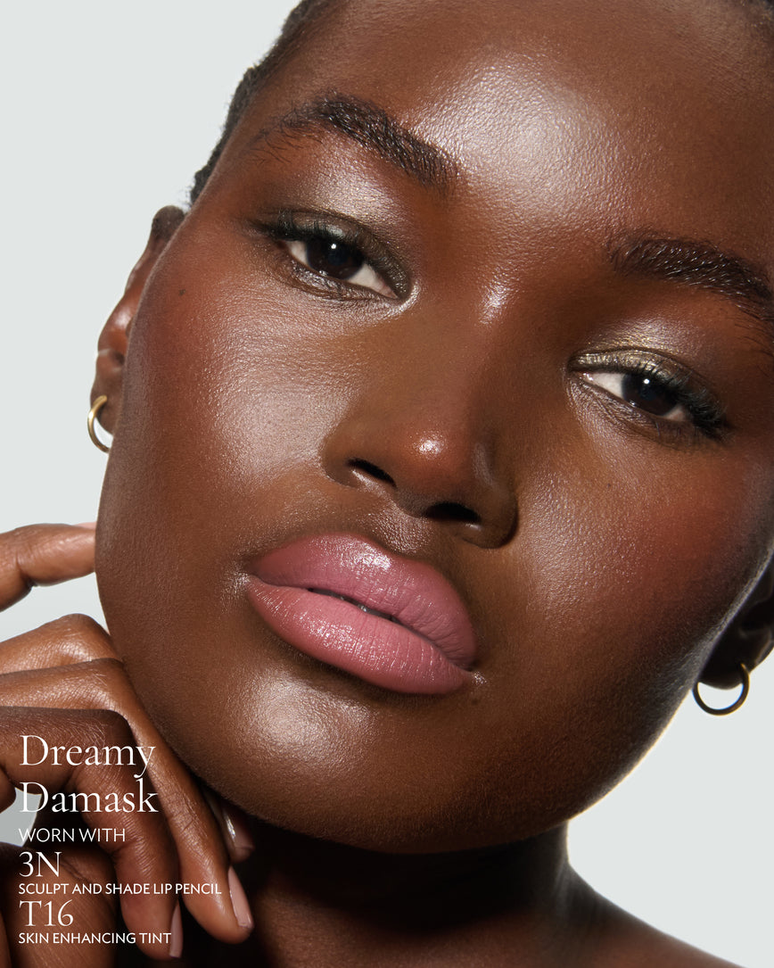 Close-up of a model's face against a neutral background, wearing Dreamy Damask Rouge Experience, Sculpt and Shade Lip Pencil in 3N and T16 Skin Enhancing Tint