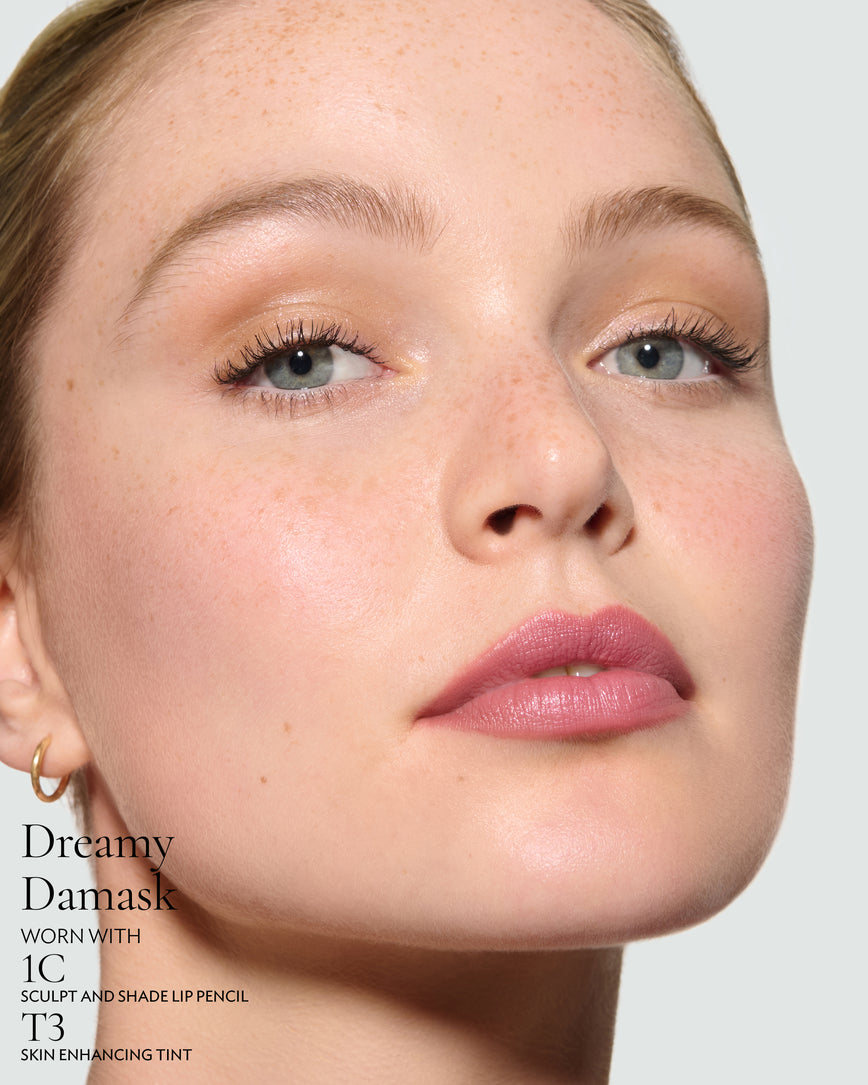 Close-up of a model's face against a neutral background, wearing Dreamy Damask Rouge Experience, Sculpt and Shade Lip Pencil in 1C and T3 Skin Enhancing Tint