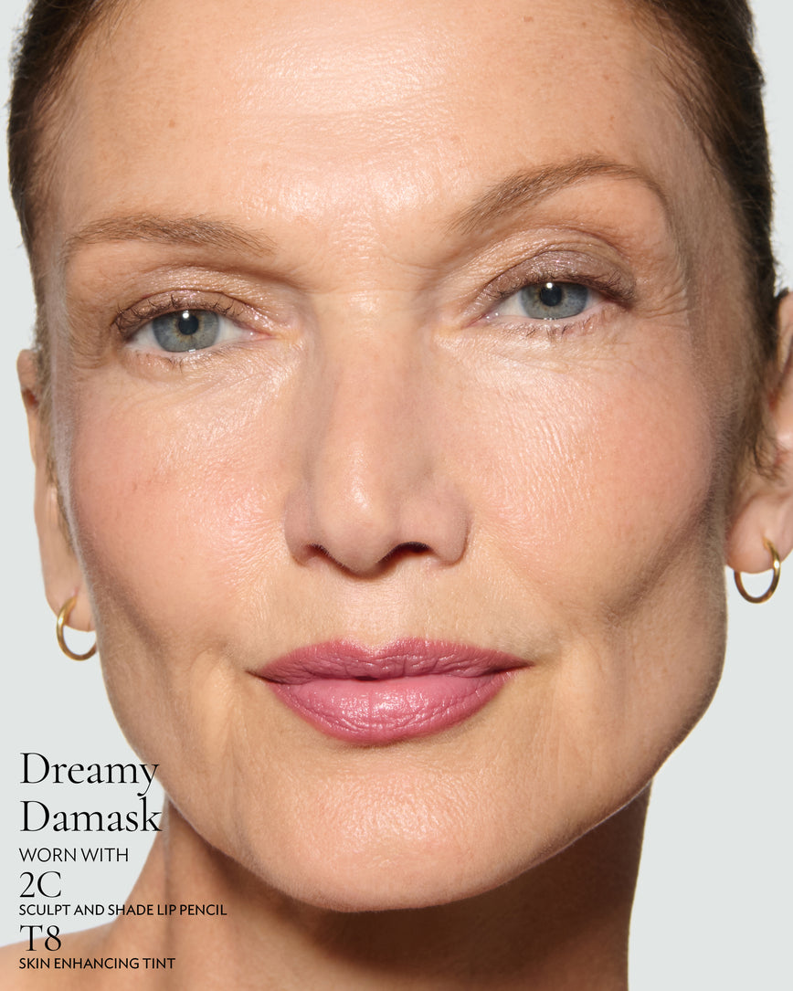 Close-up of a model's face against a neutral background, wearing Dreamy Damask Rouge Experience, Sculpt and Shade Lip Pencil in 2C and T8 Skin Enhancing Tint