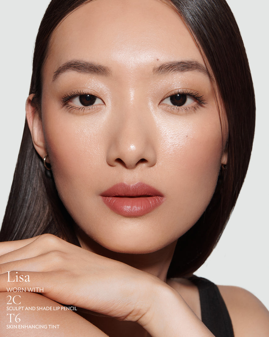 Close-up of a woman with a grey background, focusing on the lip colour - neutral pink Lisa, with notes on the 2C Sculpt and Shade Pencil and T6 Skin Enhancing Tint