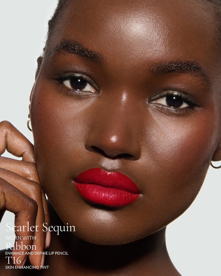 Close-up of a model's face against a neutral background, wearing Scarlet Sequin Rouge Experience, Selene Liquid Lurex, Ribbon Enhance and Define, and T16 Skin Enhancing Tint