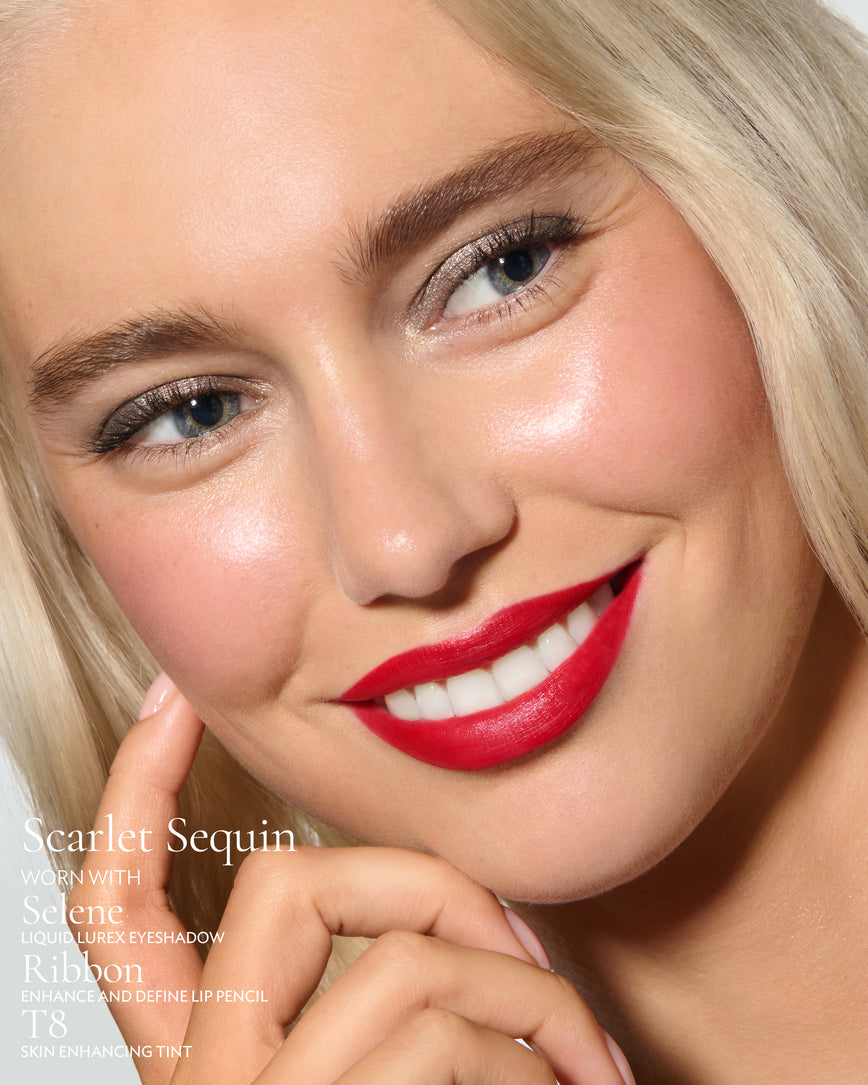 Close-up of a model's face against a neutral background, wearing Scarlet Sequin Rouge Experience, Selene Liquid Lurex, Ribbon Enhance and Define, and T8 Skin Enhancing Tint