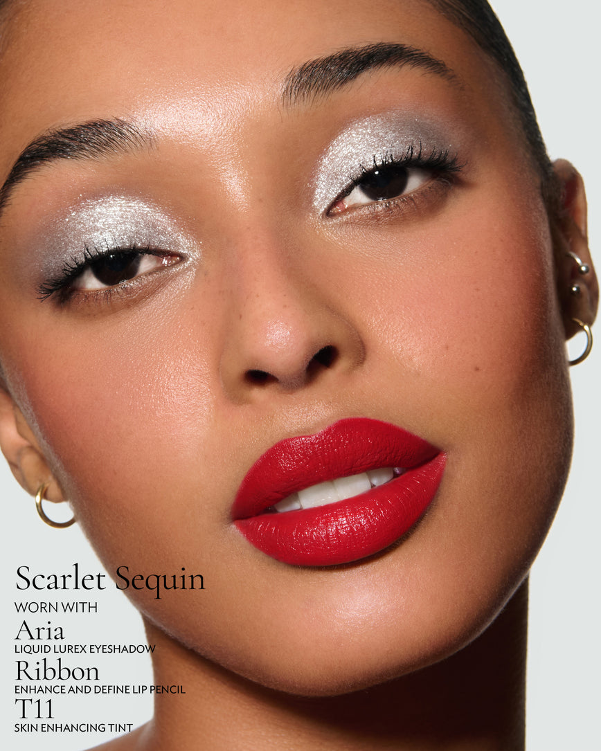 Close-up of a model's face against a neutral background, wearing Scarlet Sequin Rouge Experience, Aria Liquid Lurex, Ribbon Enhance and Define, and T11 Skin Enhancing Tint