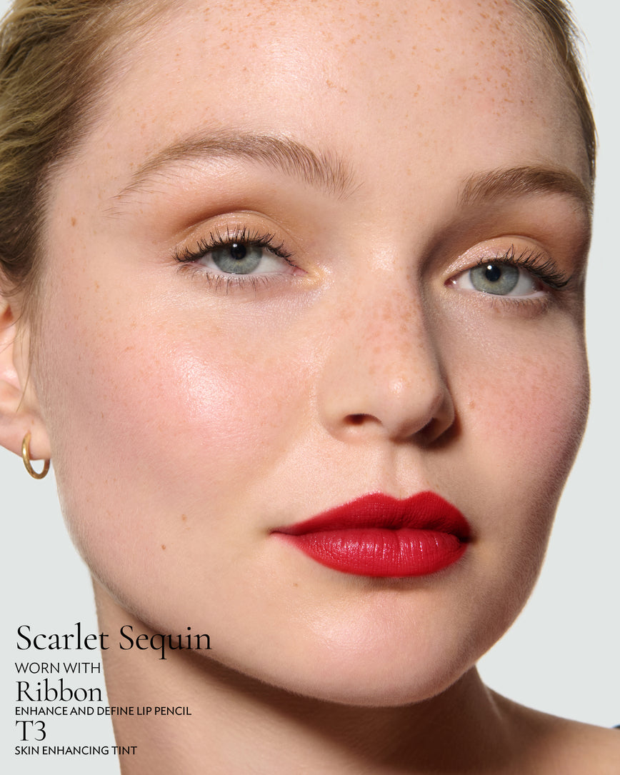 Close-up of a model's face against a neutral background, wearing Scarlet Sequin Rouge Experience, Ribbon Enhance and Define, and T3 Skin Enhancing Tint