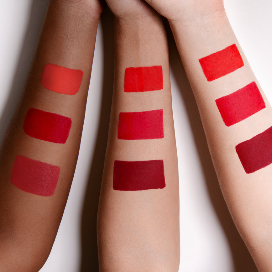 three arms with skin colours ranging from light to medium/deep with swatches of red lipstick